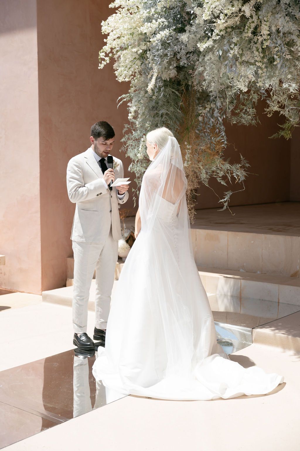 A wedding couple standing beneath white floral arrangements during their ceremony.