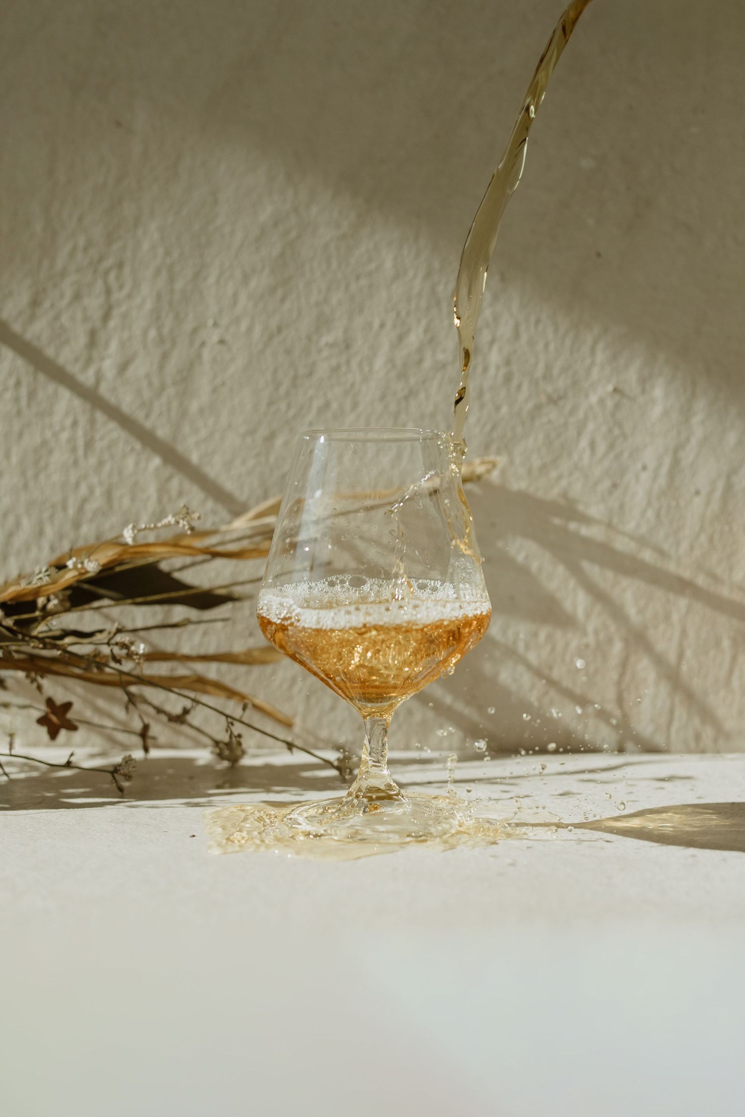 Liquid splashing into wine glass against textured wall with dramatic shadows.