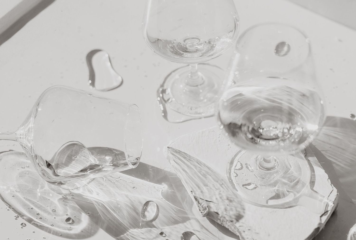 High-key still life of crystal glasses and ice cubes on white surface.