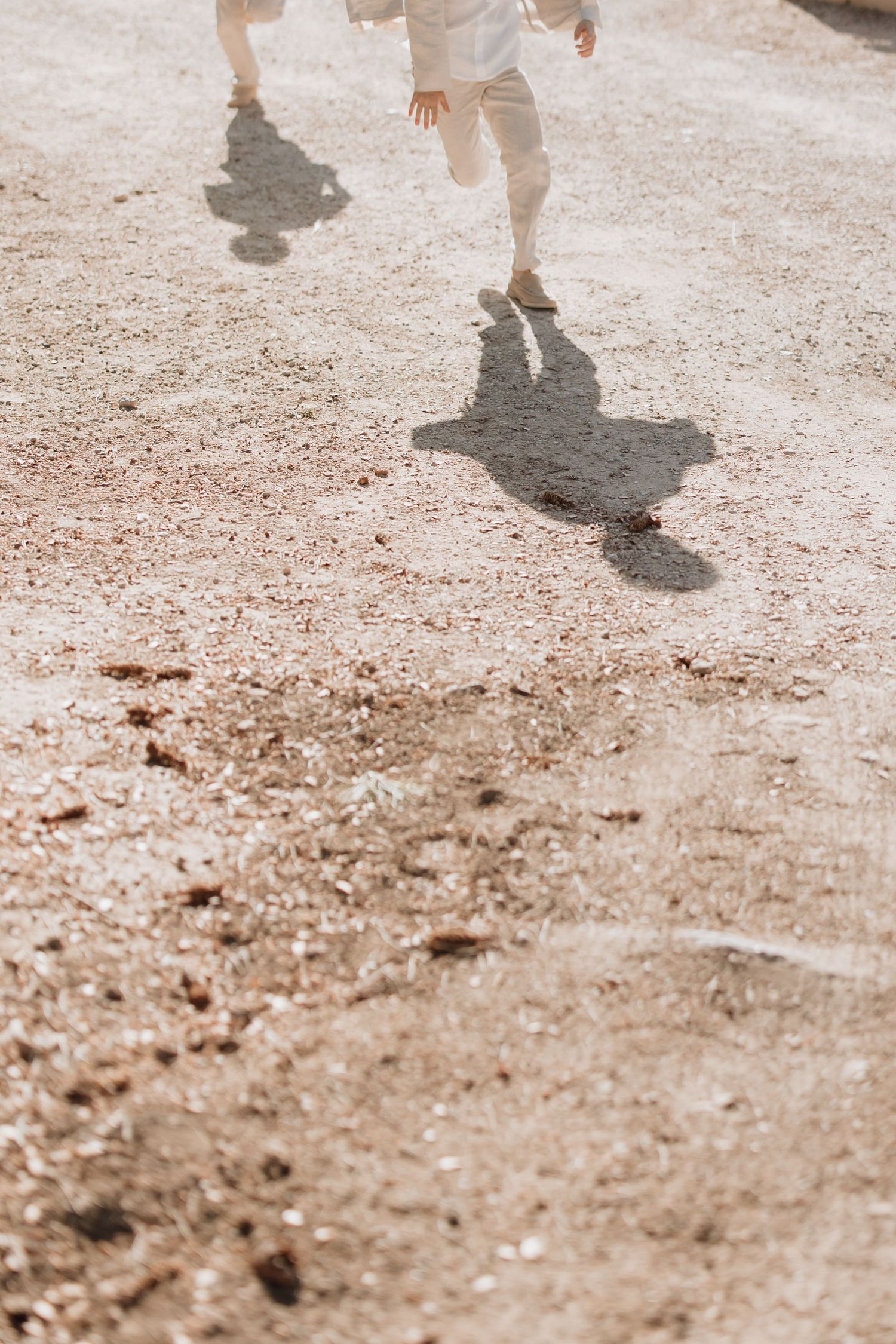 Runner's legs and shadows moving along a dusty trail on a sunny day, creating dramatic silhouettes on dirt path.