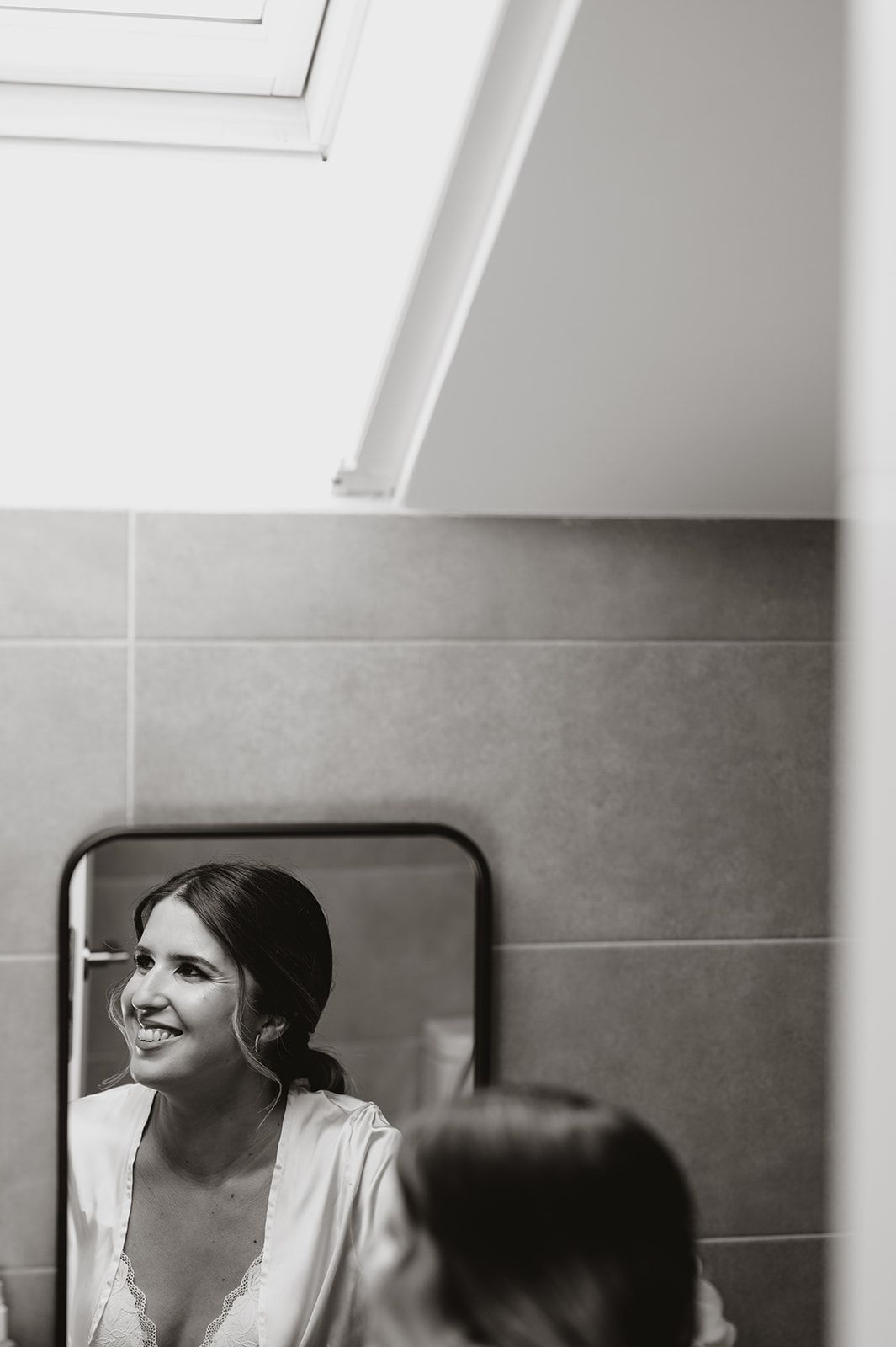 Black and white reflection of someone smiling in a bathroom mirror.