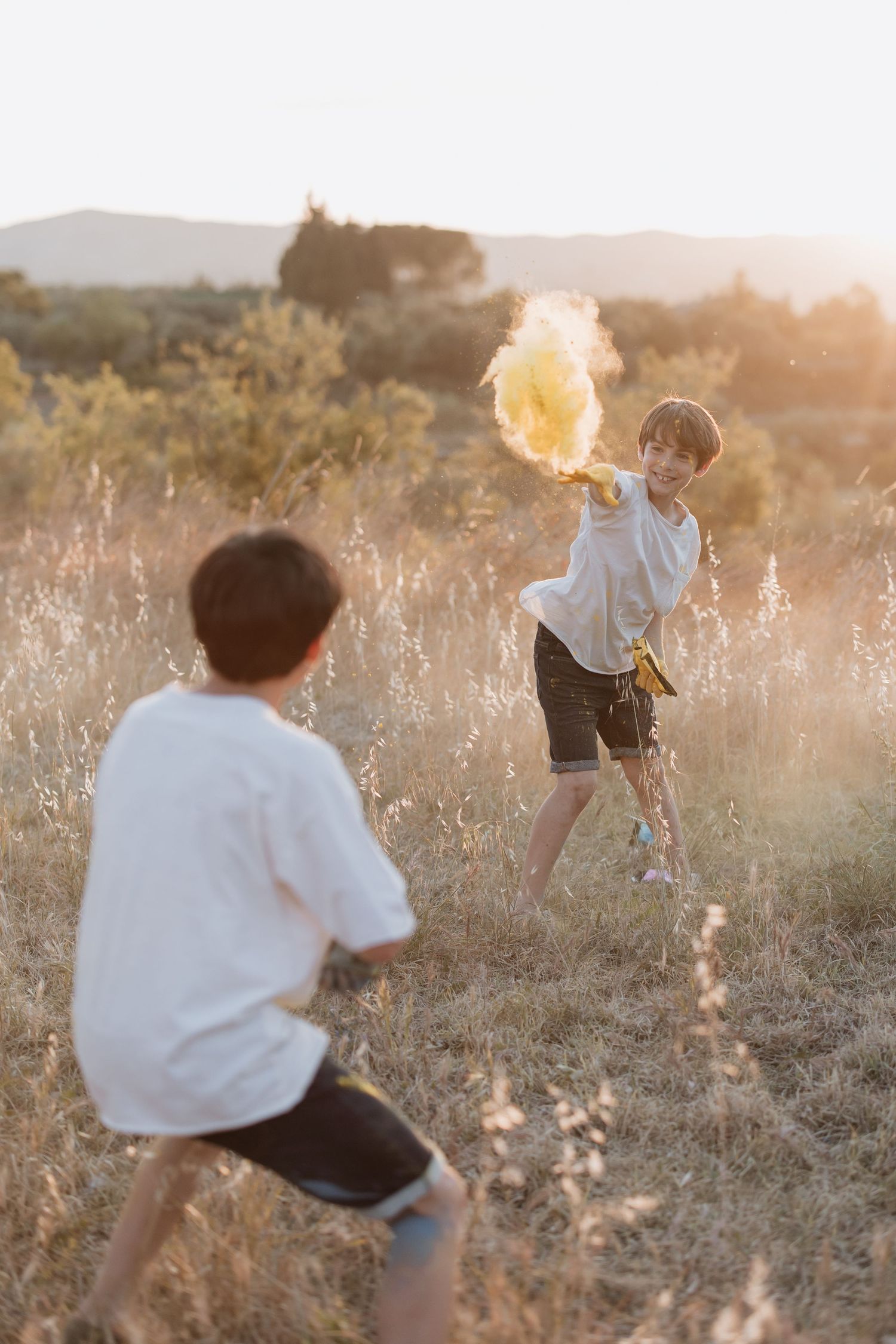Two people playing together in a sunlit field at golden hour throwing something in the air.