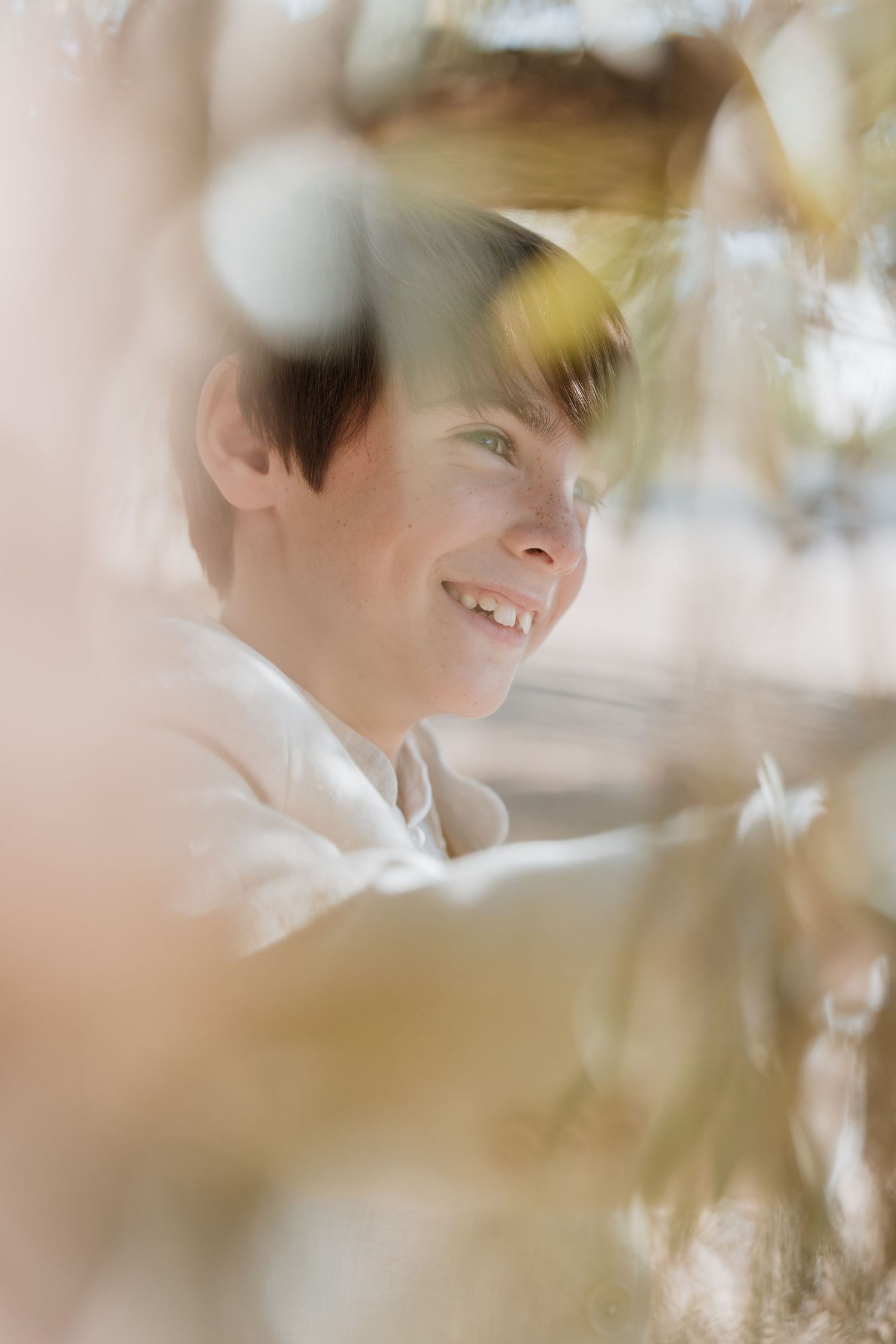 Soft focus portrait with dreamy bokeh effect showing a gentle smile through blurred foreground elements.