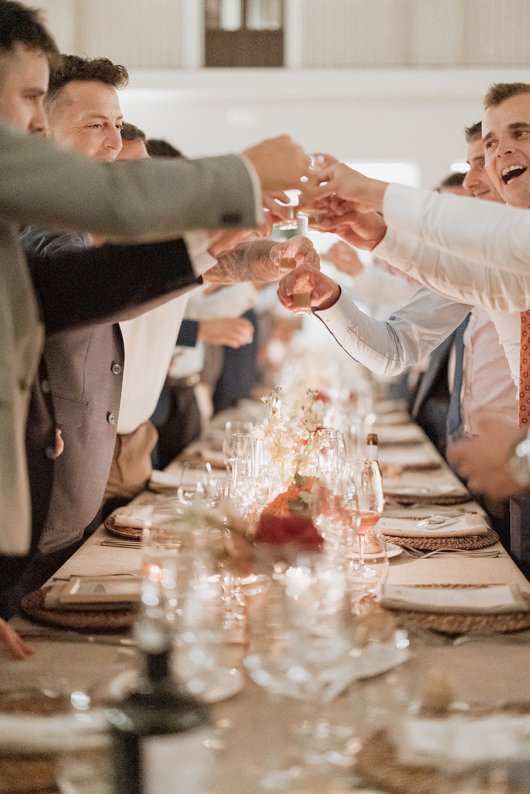 Wedding guests toasting with champagne glasses across elegant dinner table.