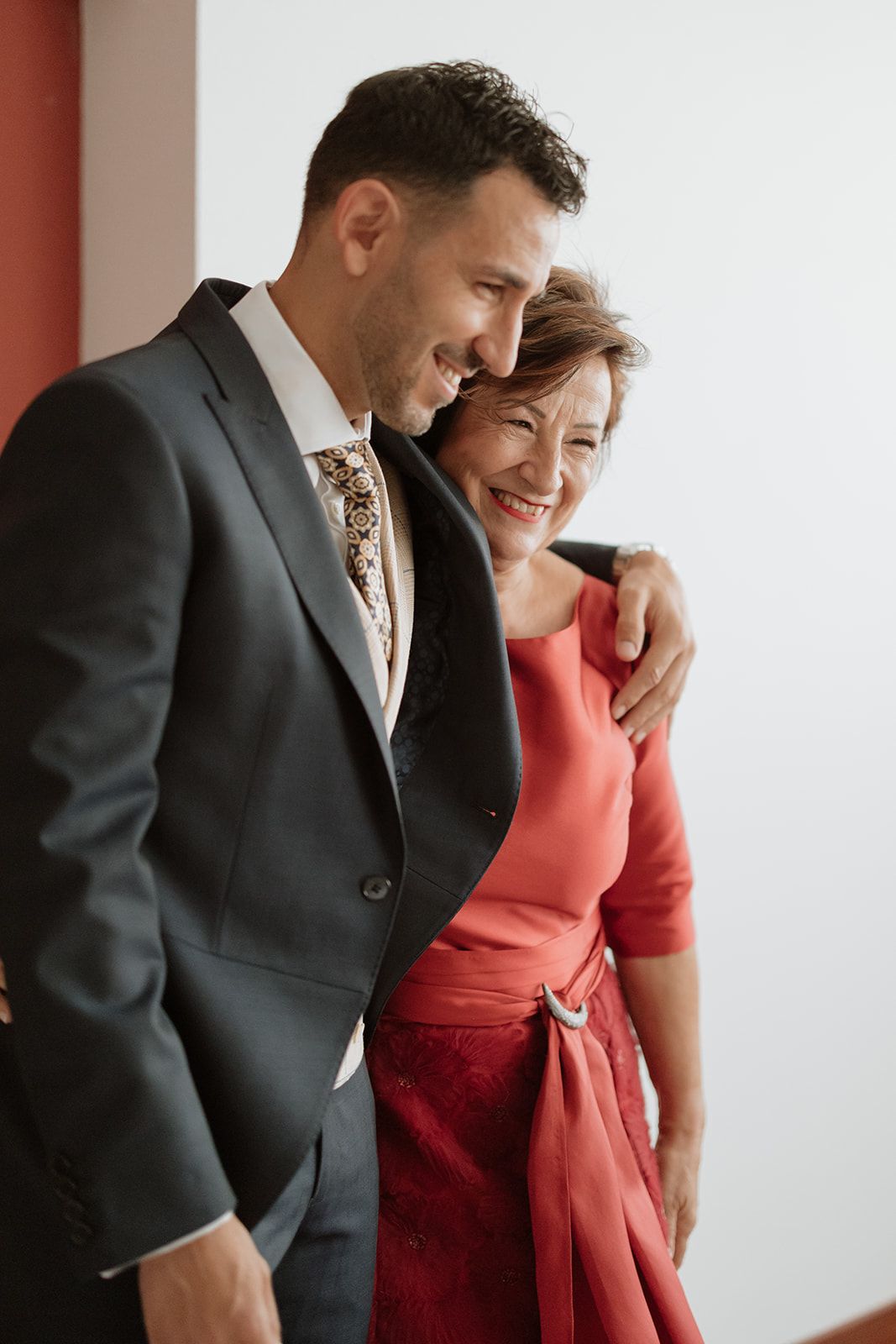 An intimate moment shared between two formally dressed people smiling and embracing at a wedding.