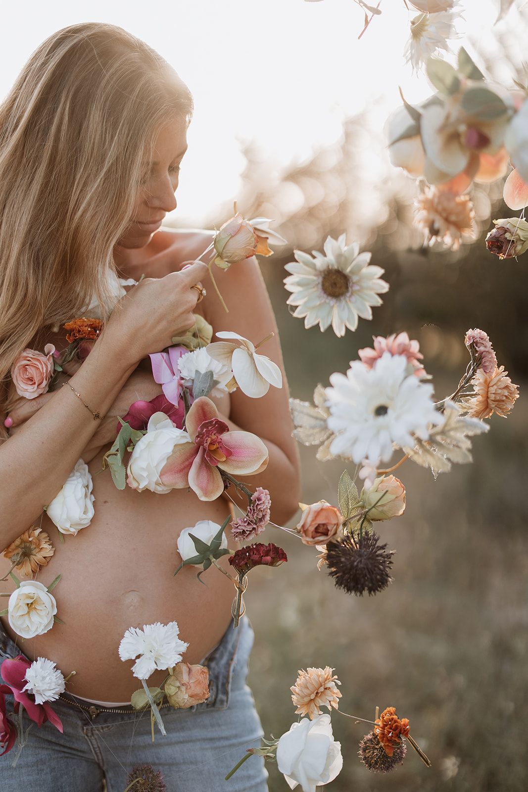 An artistic maternity portrait with delicate flowers arranged on the belly in warm evening light.