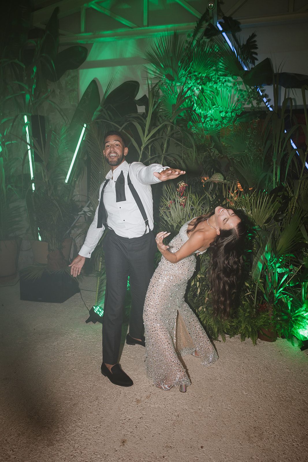 Couple performing a dramatic dance dip move at a party with green lighting and palm decorations.