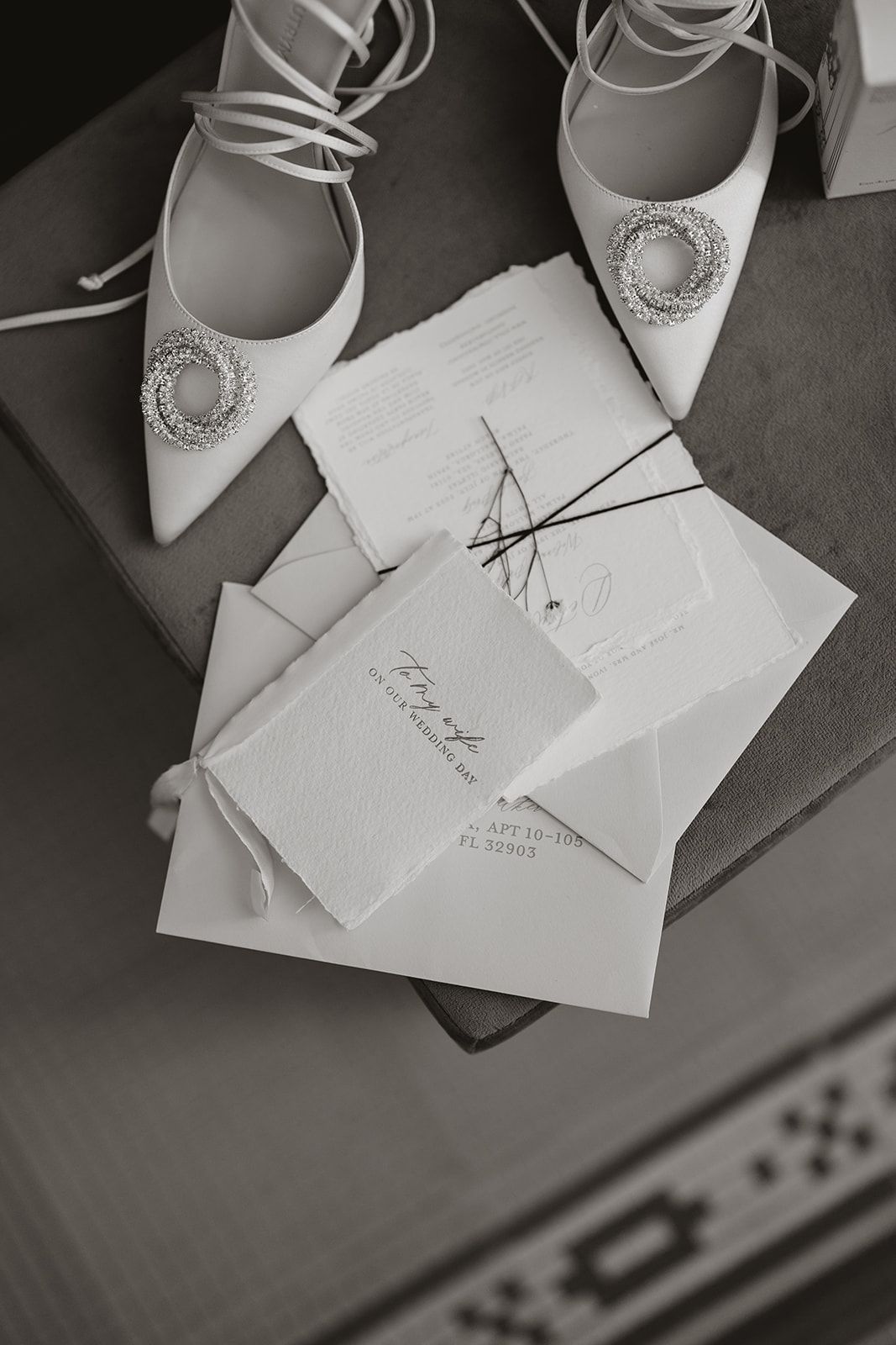 Elegant white bridal shoes with crystal embellishments next to wedding invitations.