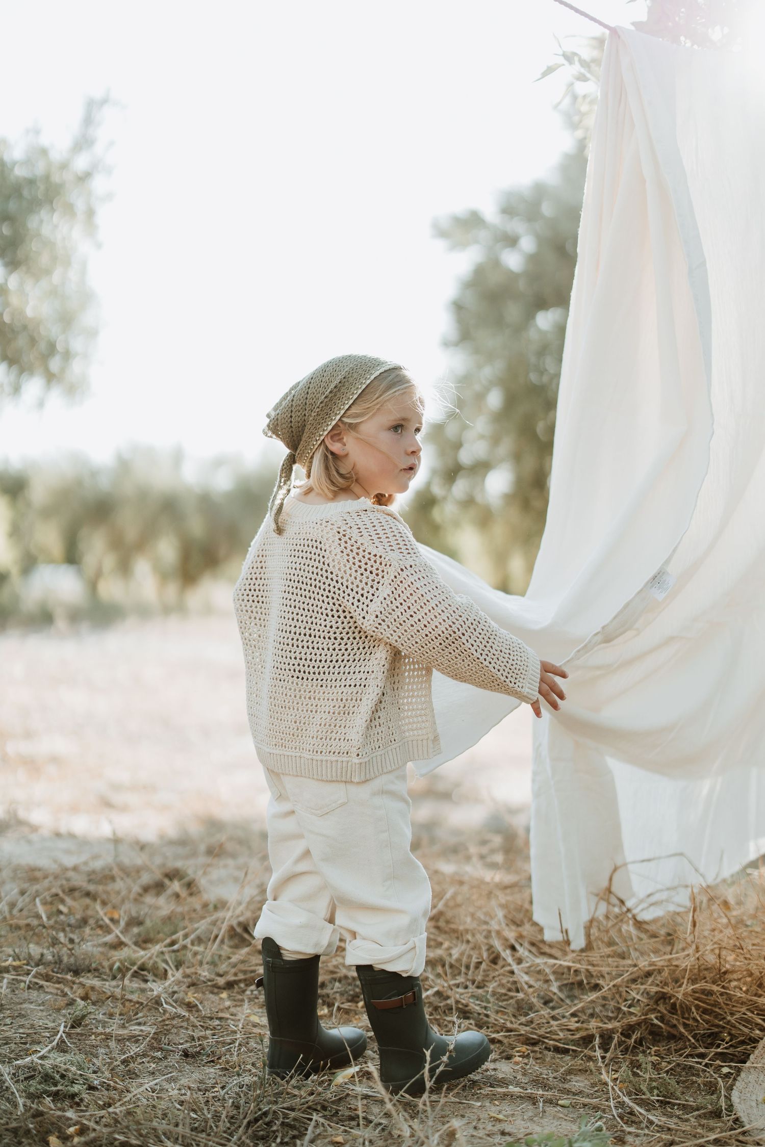 Small figure in knit sweater touches white linens hanging on outdoor clothesline.