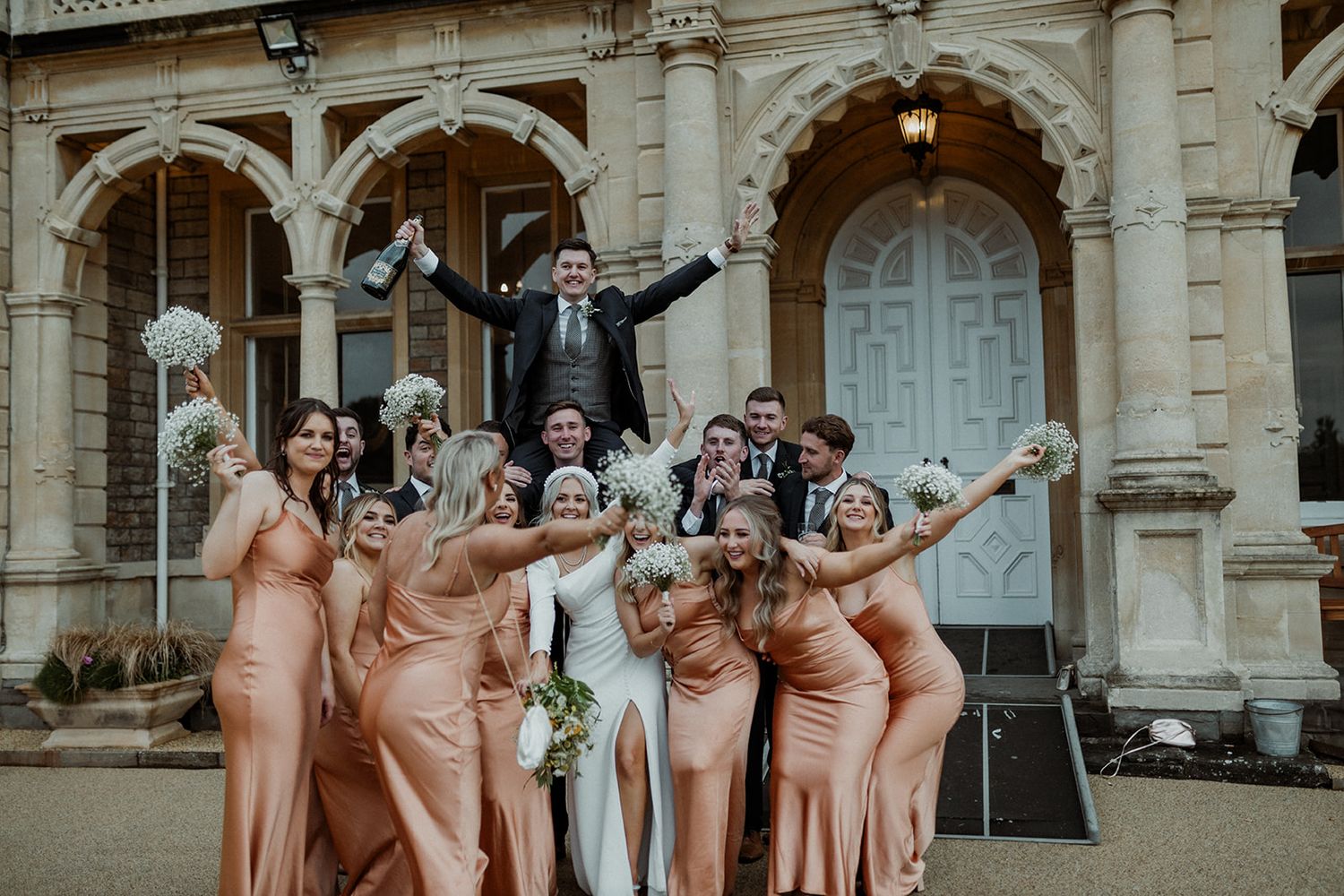 Wedding party celebrating outside a historic building with bridesmaids in matching peach dresses.