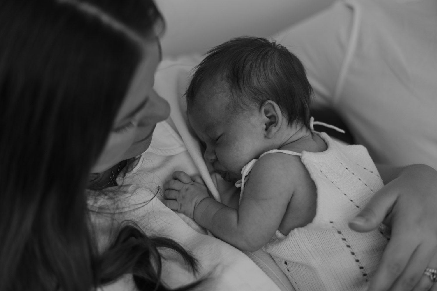 Black and white photo of a baby sleeping peacefully in bed while being touched gently.