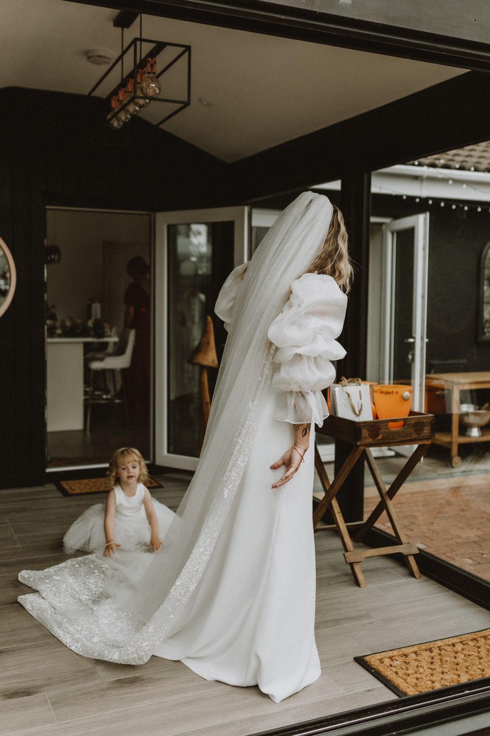 Wedding dress trail elegantly draped across modern wooden floor with child playing nearby.