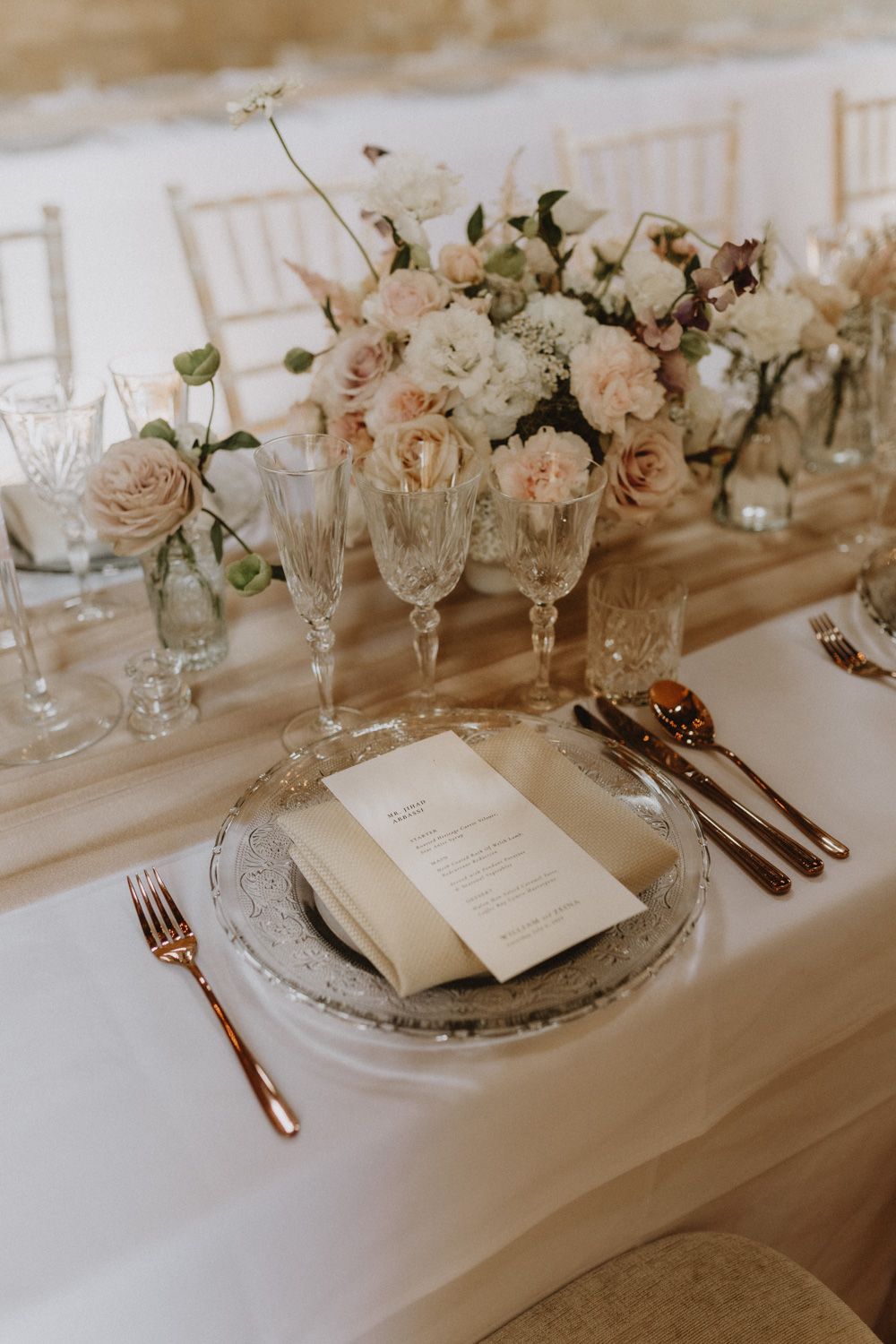 Elegant wedding table setting with blush roses, crystal glasses, and menu cards.