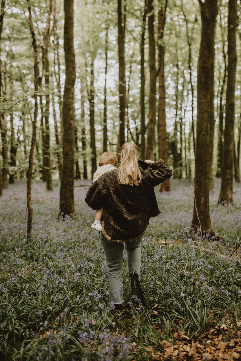 Person walking through magical woodland filled with purple wildflowers and tall trees.