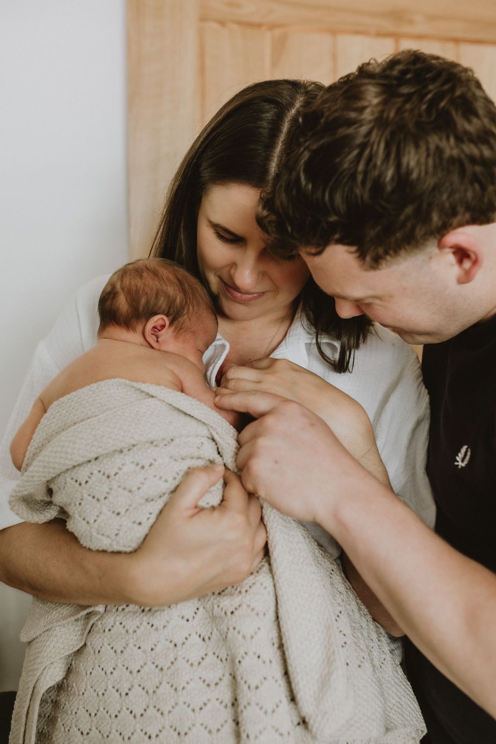 Family sharing an intimate moment with their newborn wrapped in a knit blanket.