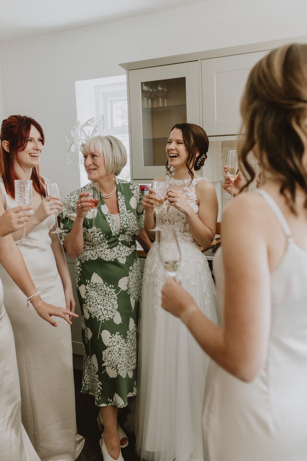 Wedding party sharing celebratory drinks and laughter in a bright interior space.