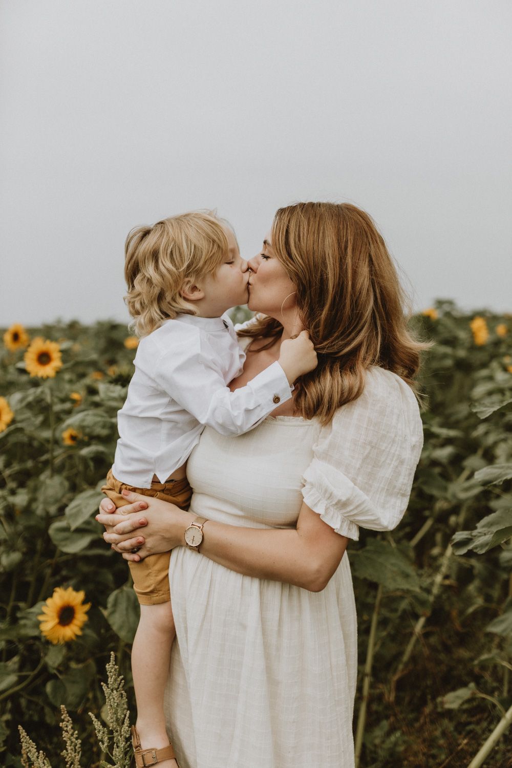Sweet moment between parent and toddler in sunflower field wearing white clothing.