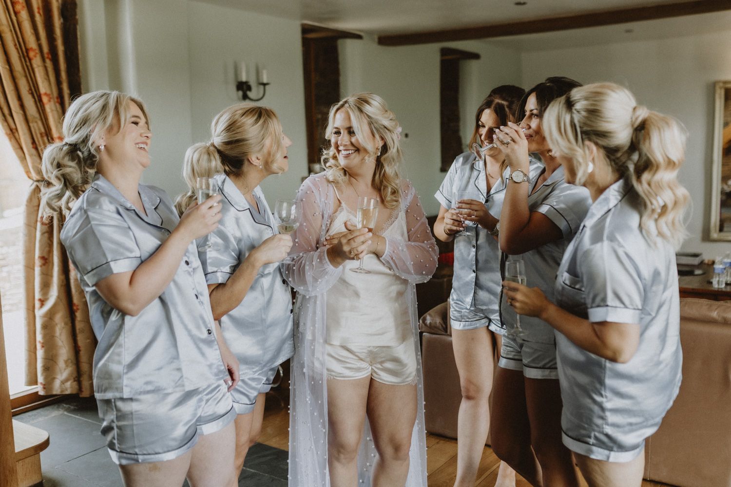 Wedding party getting ready in matching light blue robes in a sunlit room.