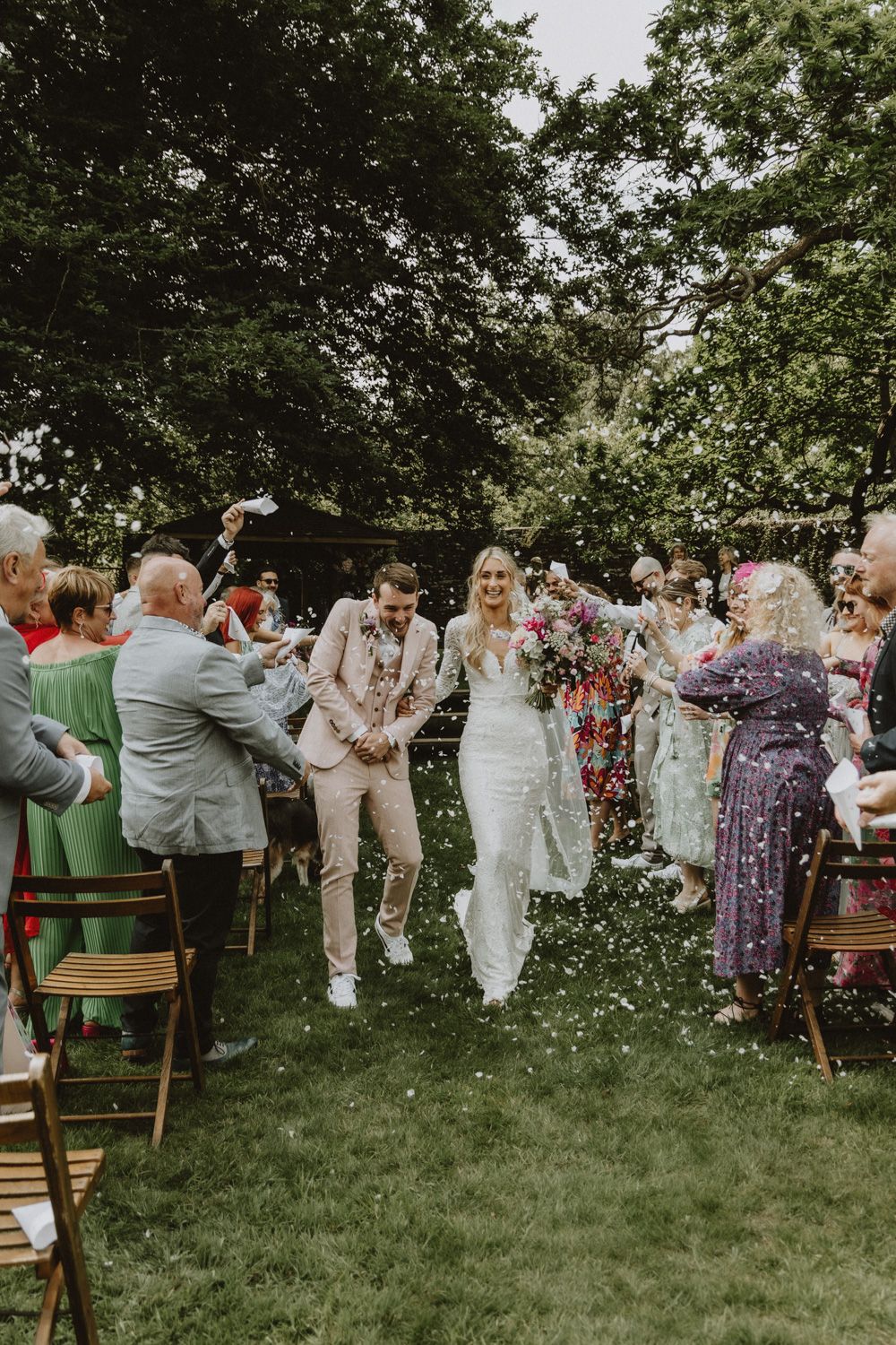 Outdoor wedding reception setup with wooden chairs on a green lawn.
