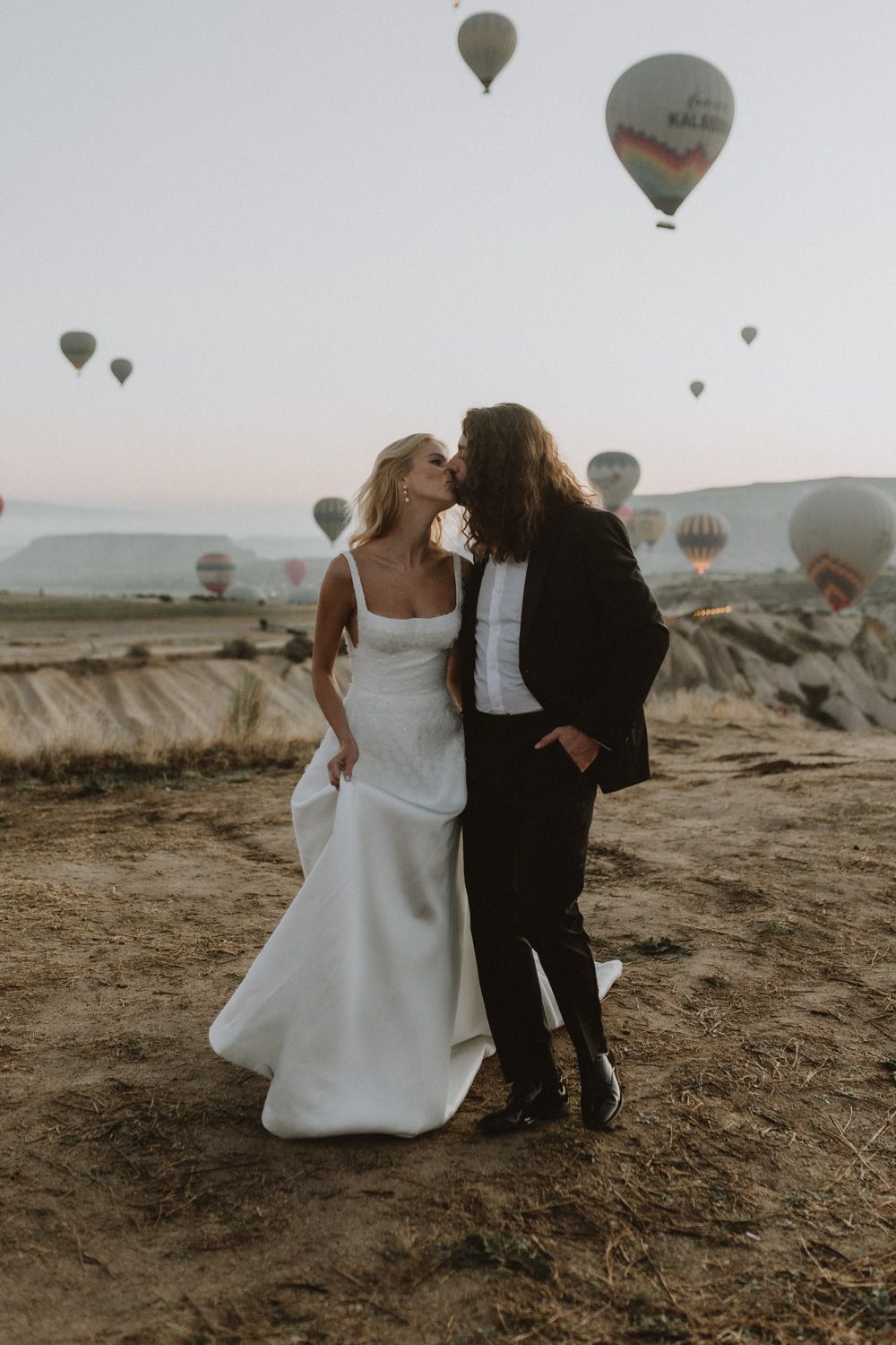 Romantic desert photoshoot with hot air balloons drifting in the morning sky.