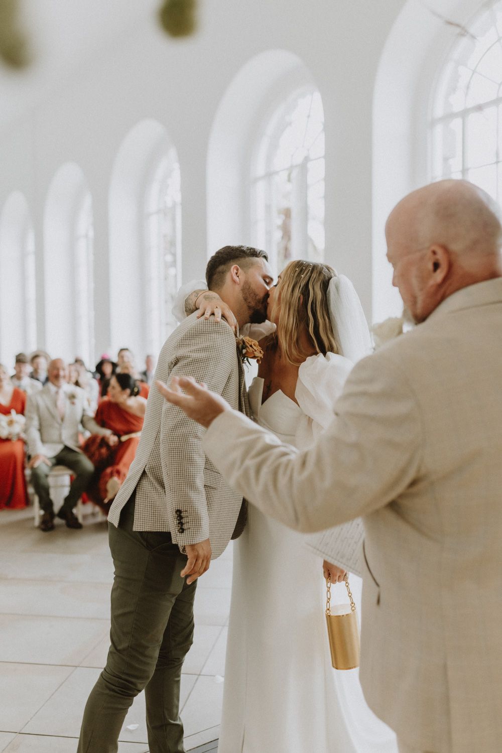 Wedding celebration in bright arched gallery with guests in red dresses and light suits.
