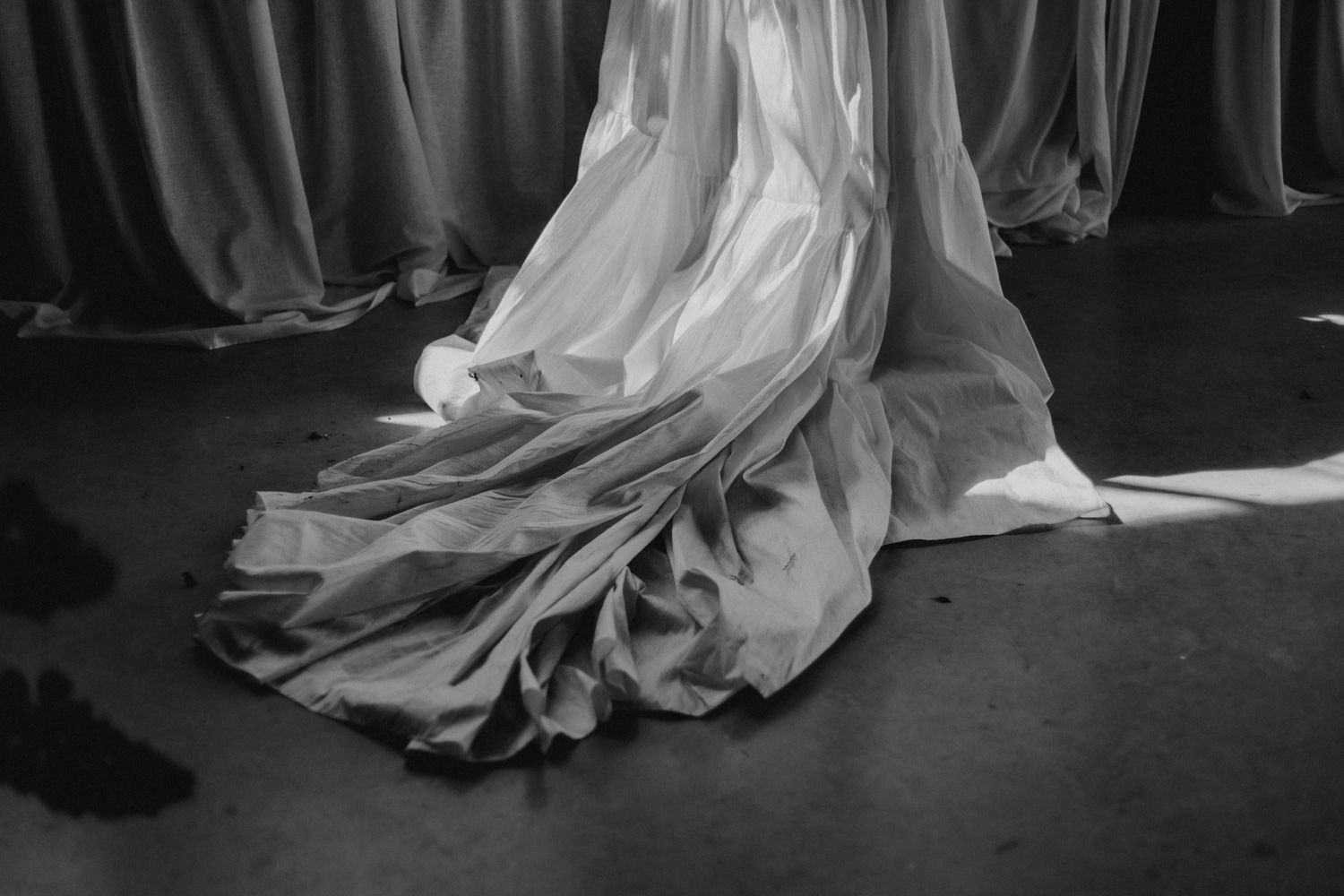 Black and white photograph of flowing wedding dress train trailing on the floor.