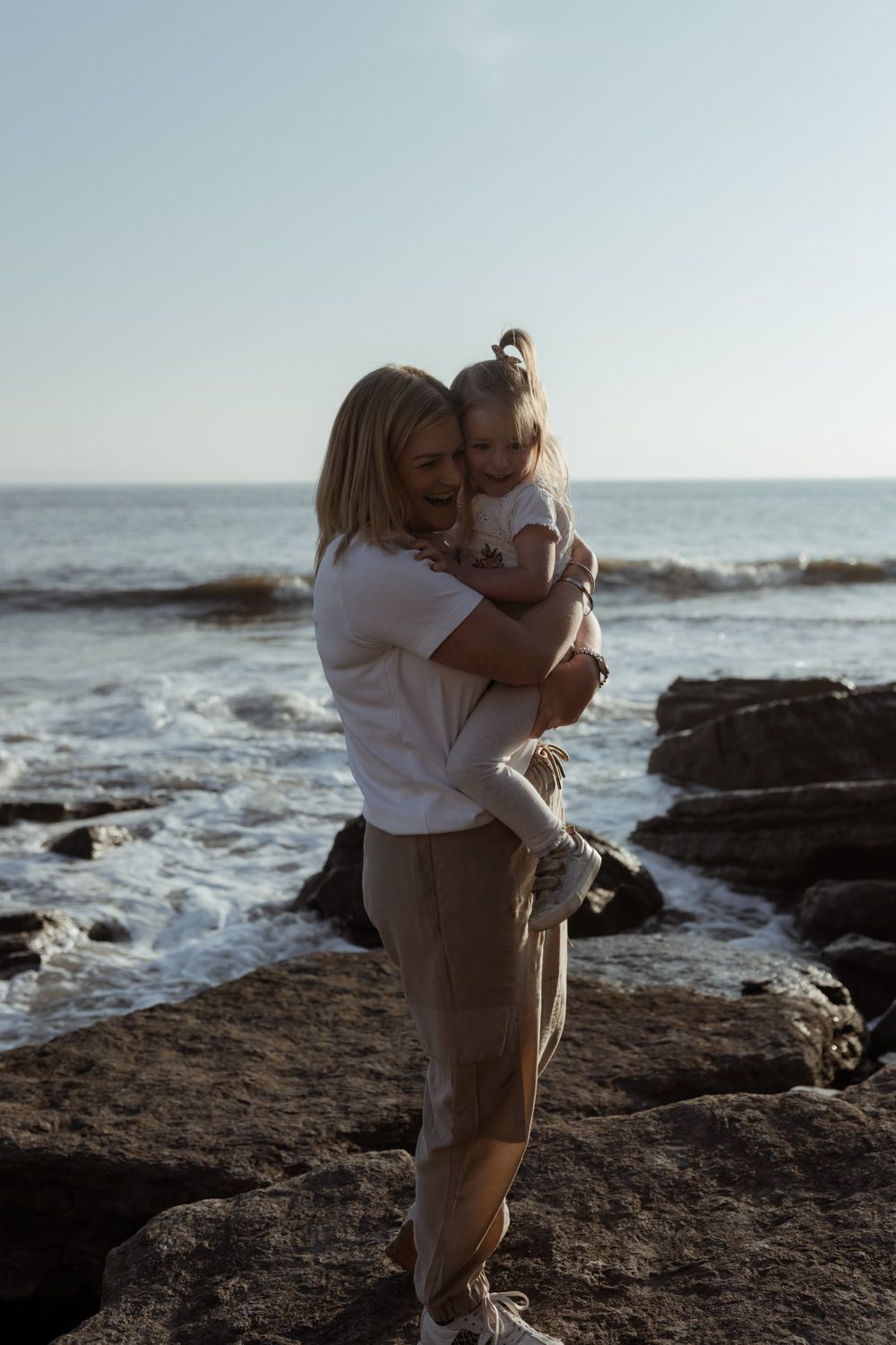 A tender embrace between parent and child on coastal rocks at sunset.