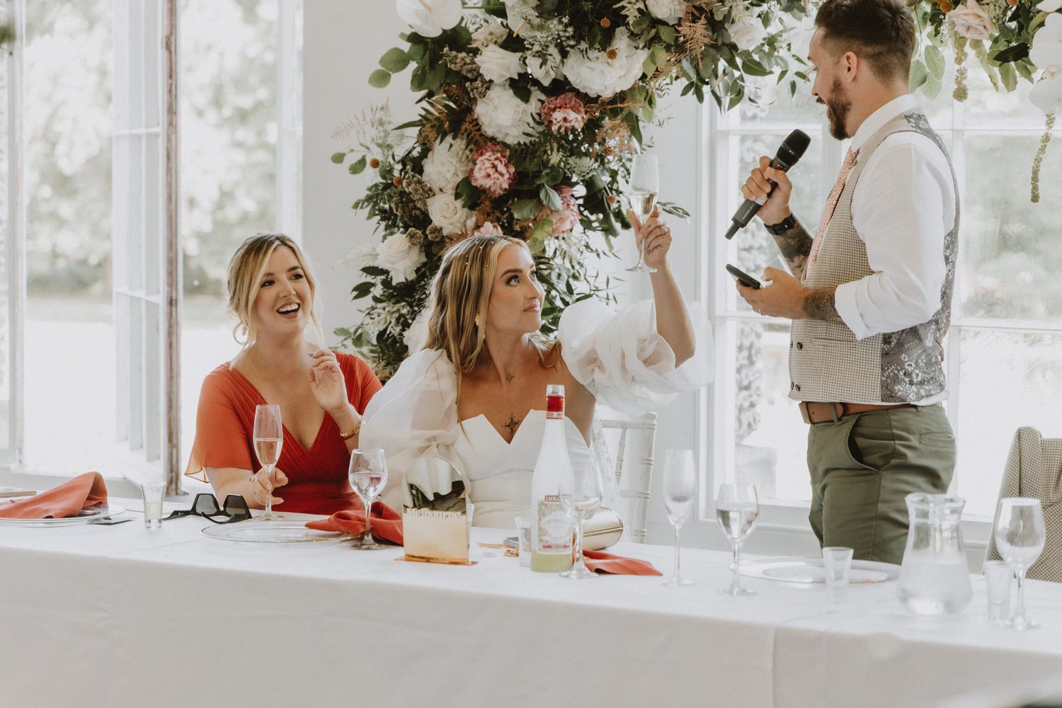 Wedding reception celebration with elegant floral arrangements and table settings in a bright white room.
