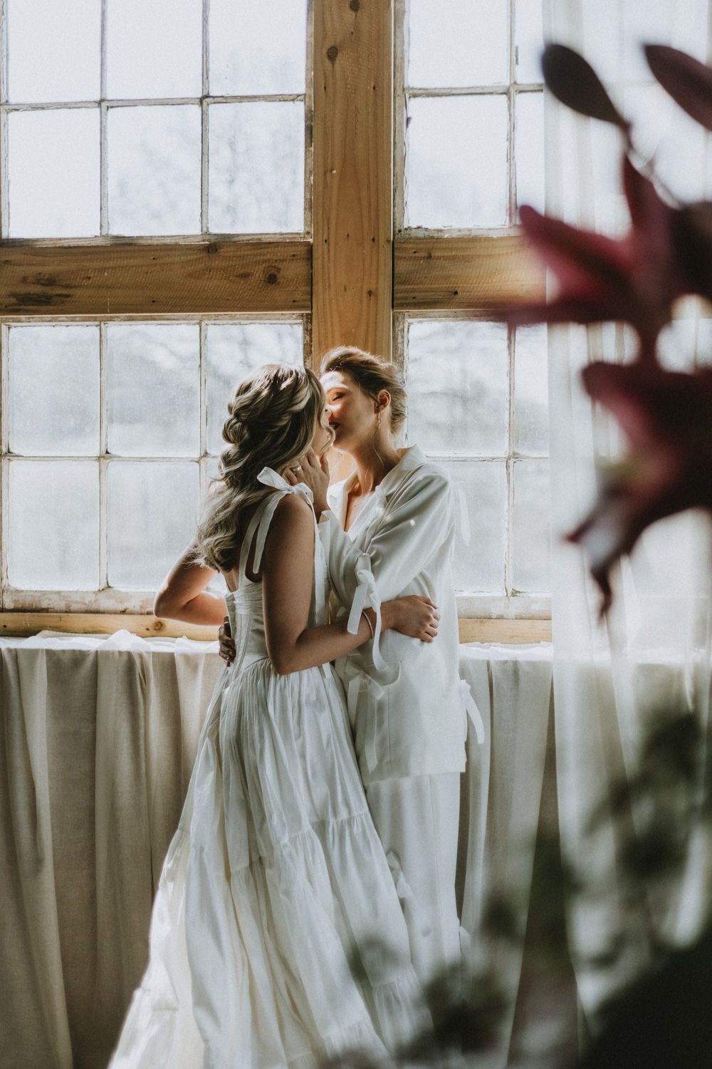 An intimate wedding moment captured by a window with delicate red flowers in the foreground.