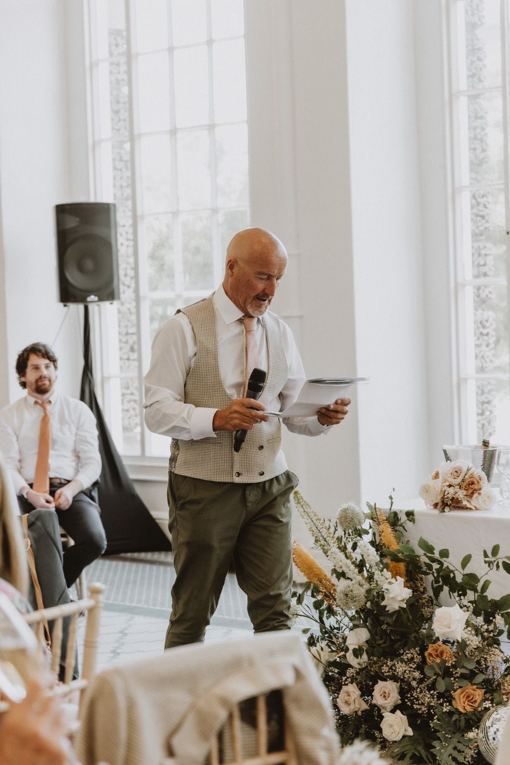 Wedding reception setup in a bright white room with floral centerpieces and natural lighting.