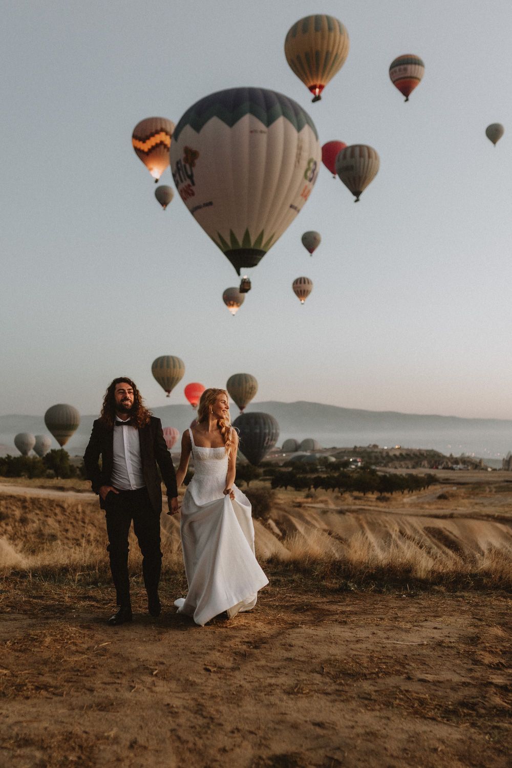 Wedding photo session with multiple hot air balloons floating in the desert landscape background.