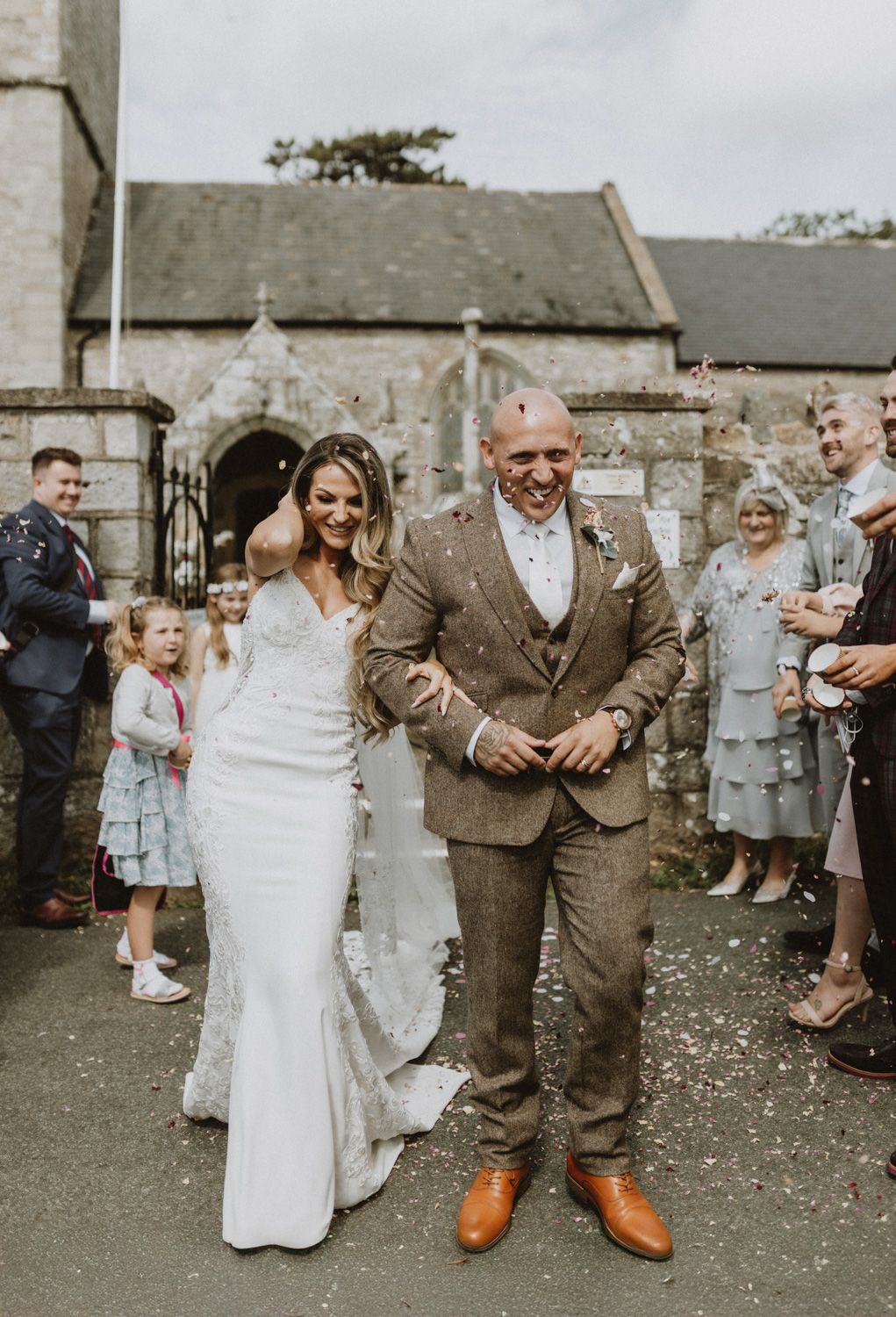 Wedding party and guests gathering outside a rustic stone building throwing confetti.