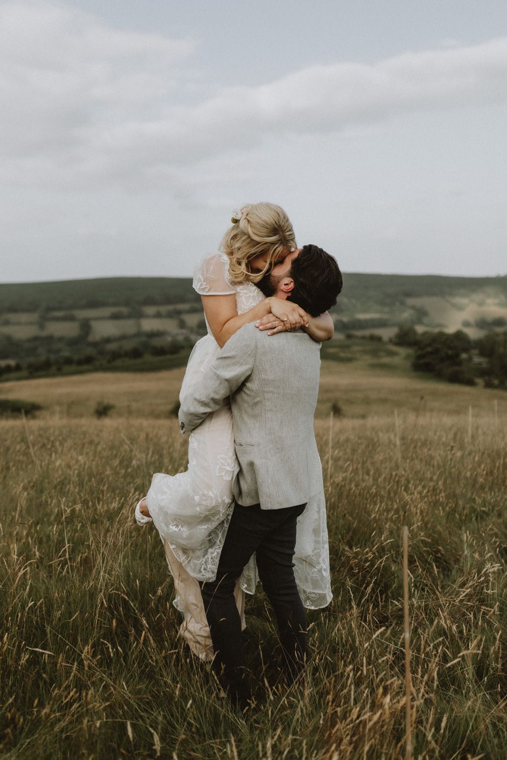 A romantic embrace between newlyweds on a hilltop overlooking rolling green countryside.