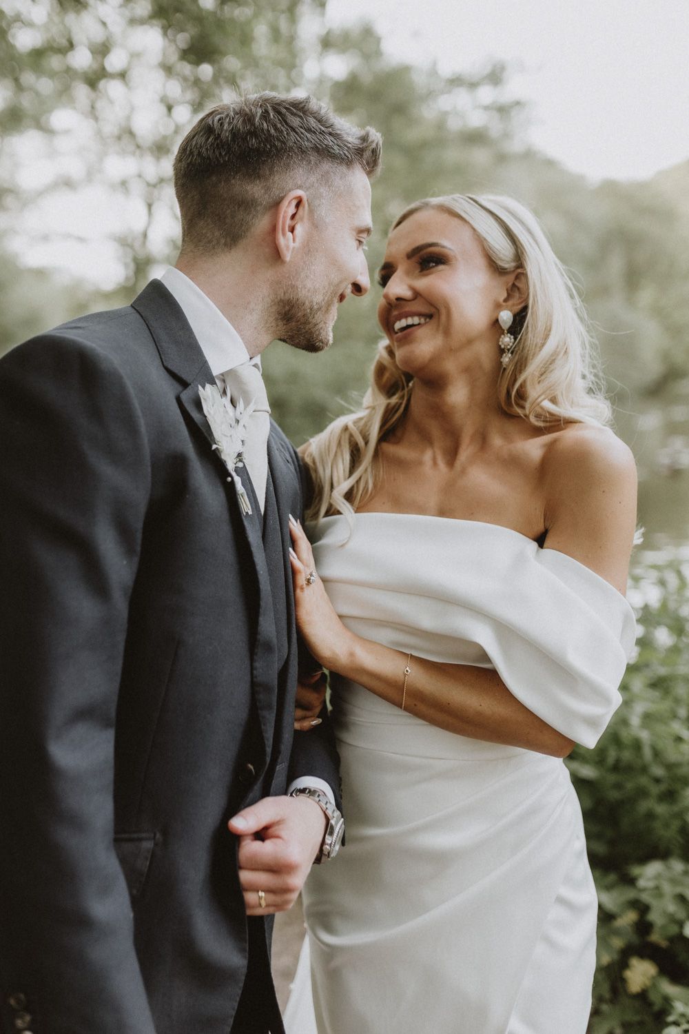 Intimate moment between newlyweds in elegant attire among garden greenery.