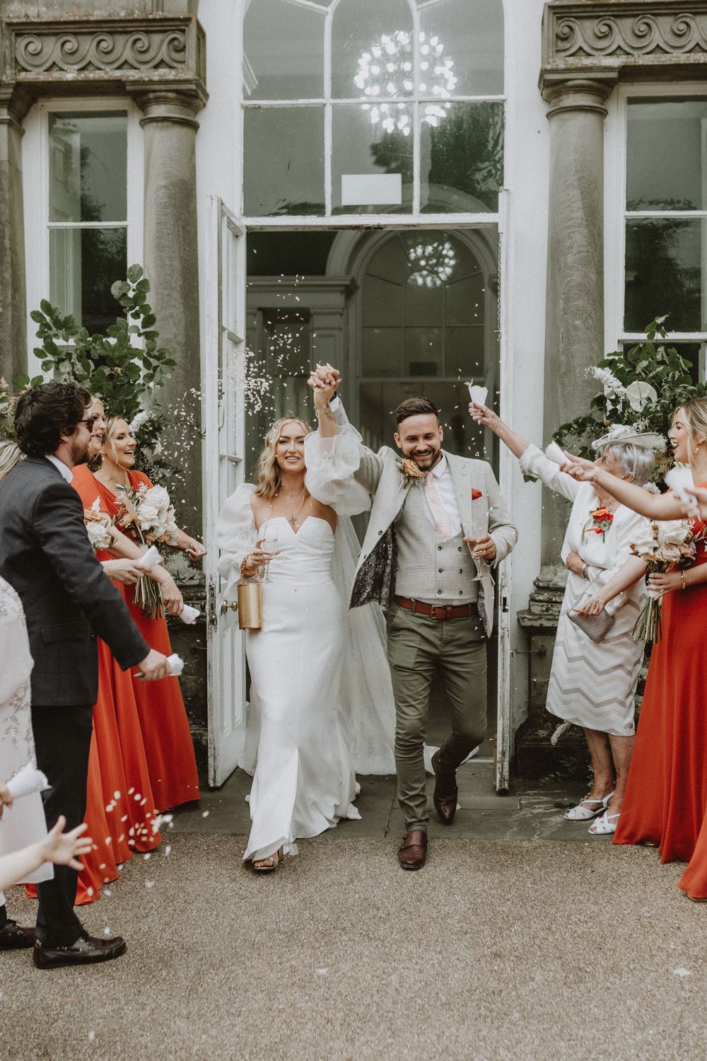 Wedding couple celebrates with guests in formal attire as they exit historical stone building.
