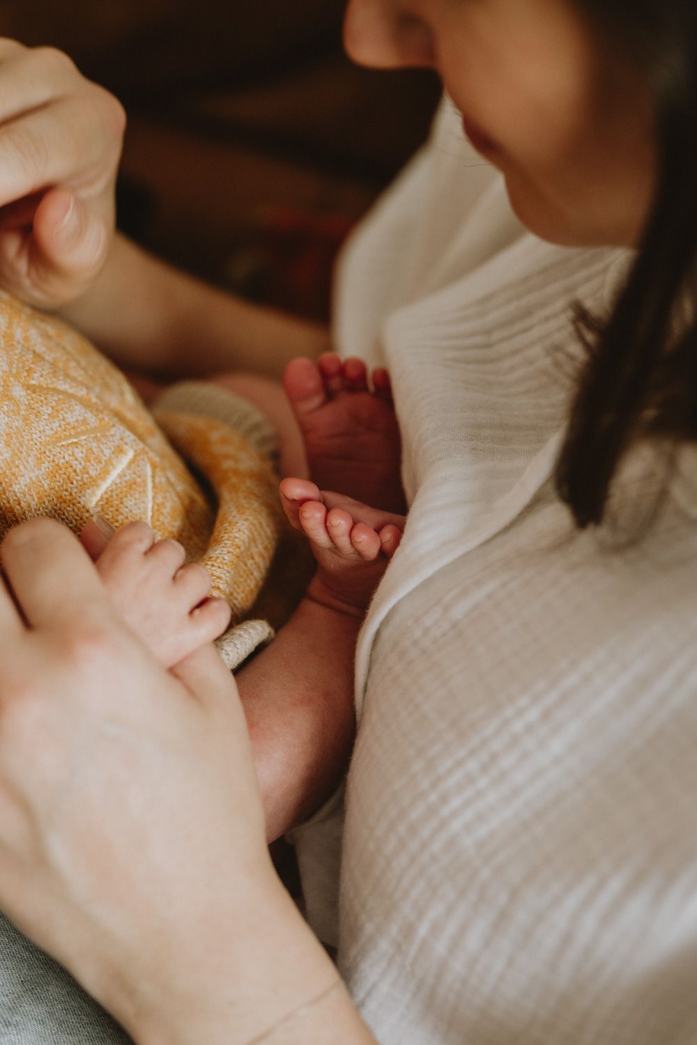 Gentle hands holding and cradling a newborn baby wrapped in white.