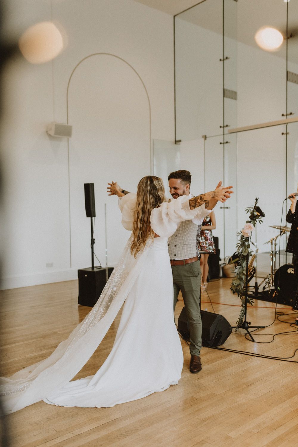 Wedding couple dancing in bright indoor venue with musical equipment visible.