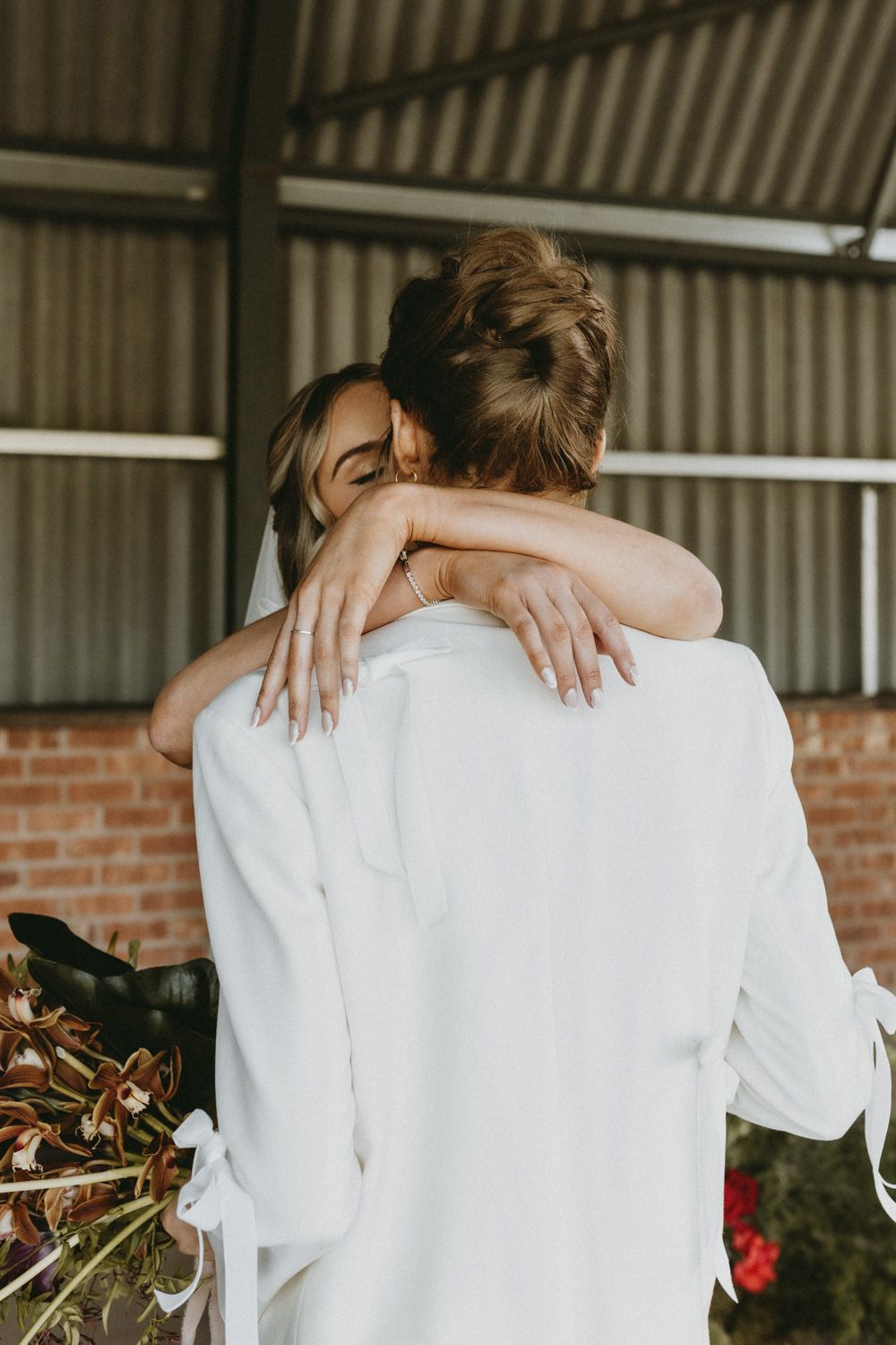 Tender moment captured between two people in white against a rustic backdrop.