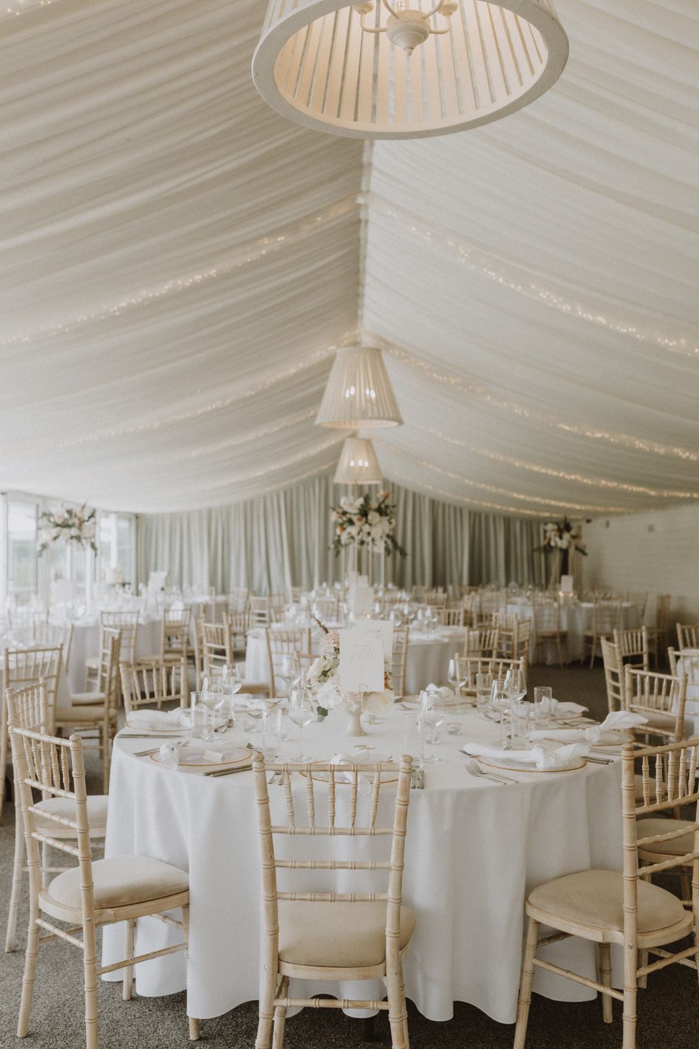 Elegant white wedding reception tent interior with round tables and chiavari chairs.