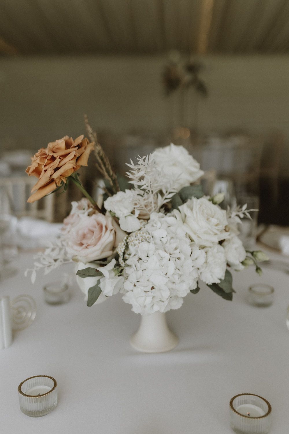 Elegant white floral centerpieces and wedding rings displayed on white tablecloth.