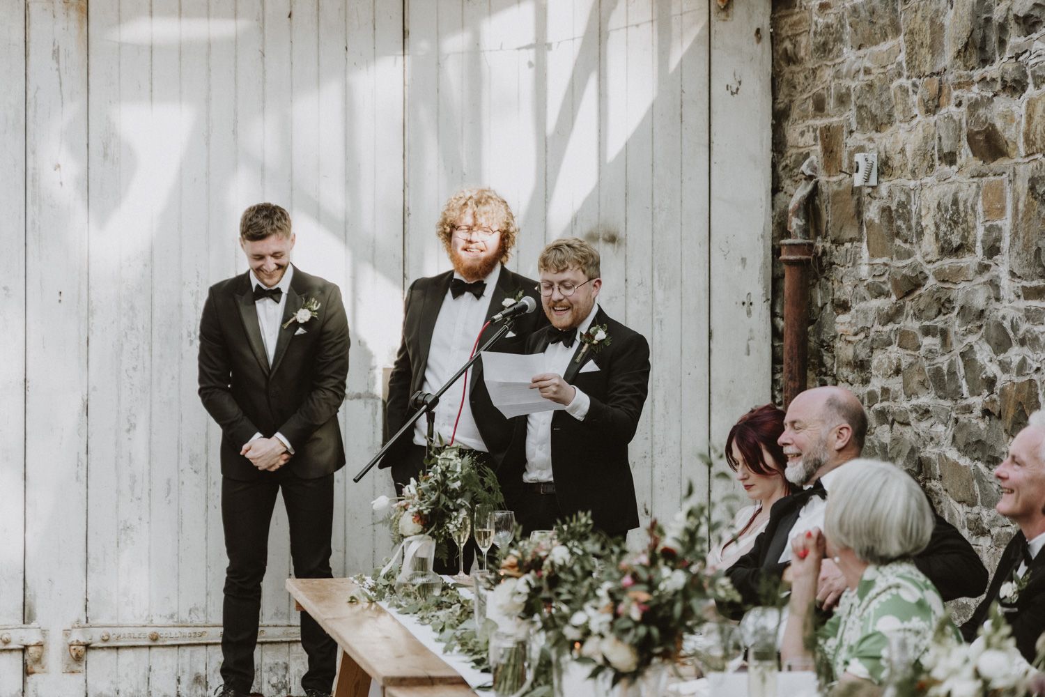 Wedding ceremony in progress against white barn door and stone wall backdrop.