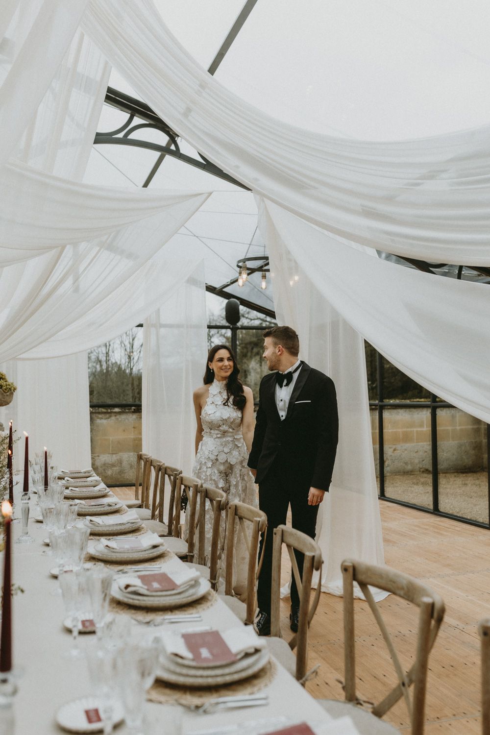 Elegant wedding reception setup with flowing white drapes and rustic wooden dining tables.