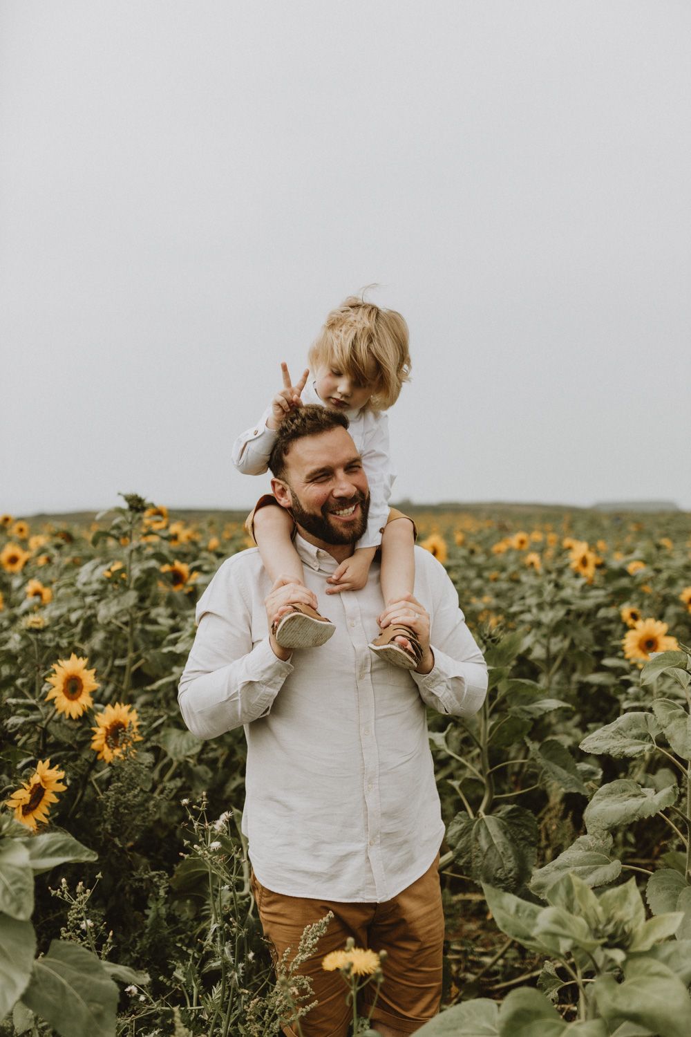 Joyful shoulders ride among towering sunflowers on overcast afternoon.