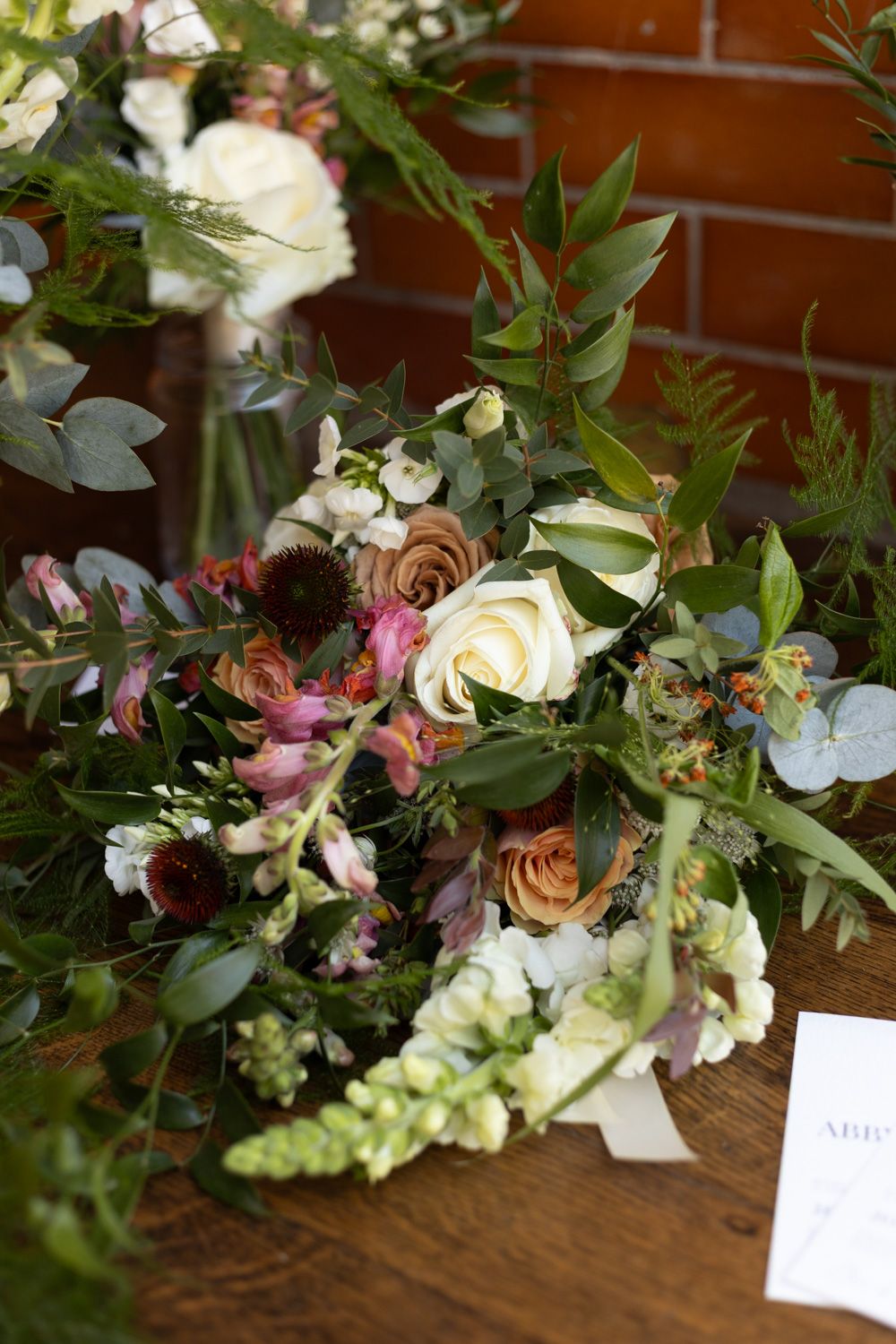 Lush wedding floral arrangement with white roses, greenery and mixed blooms on wooden surface.