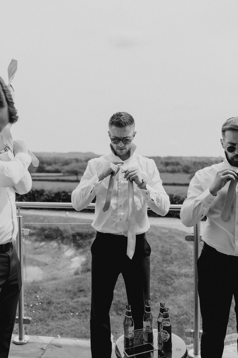 Groomsmen adjusting their ties while getting ready outdoors on a wedding day.