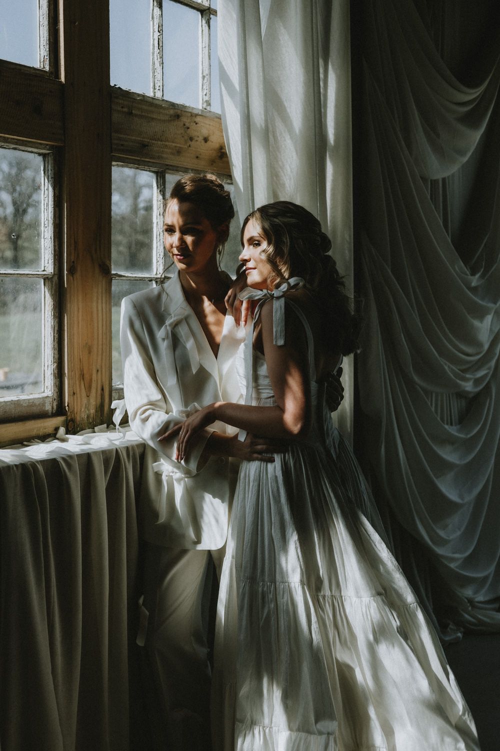 A romantic moment by a rustic window with natural light streaming through white curtains.