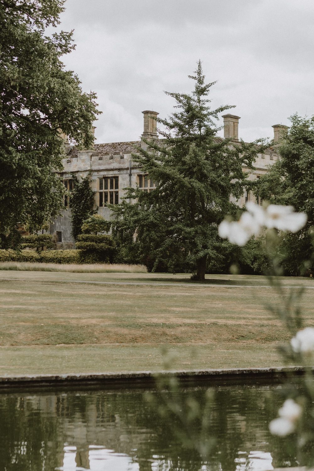 Stately manor house with reflecting pond and manicured grounds.
