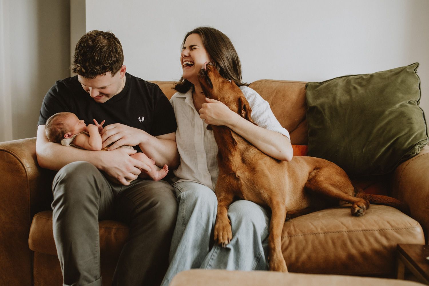 Couple and dog relaxing together on brown leather couch in modern living room.