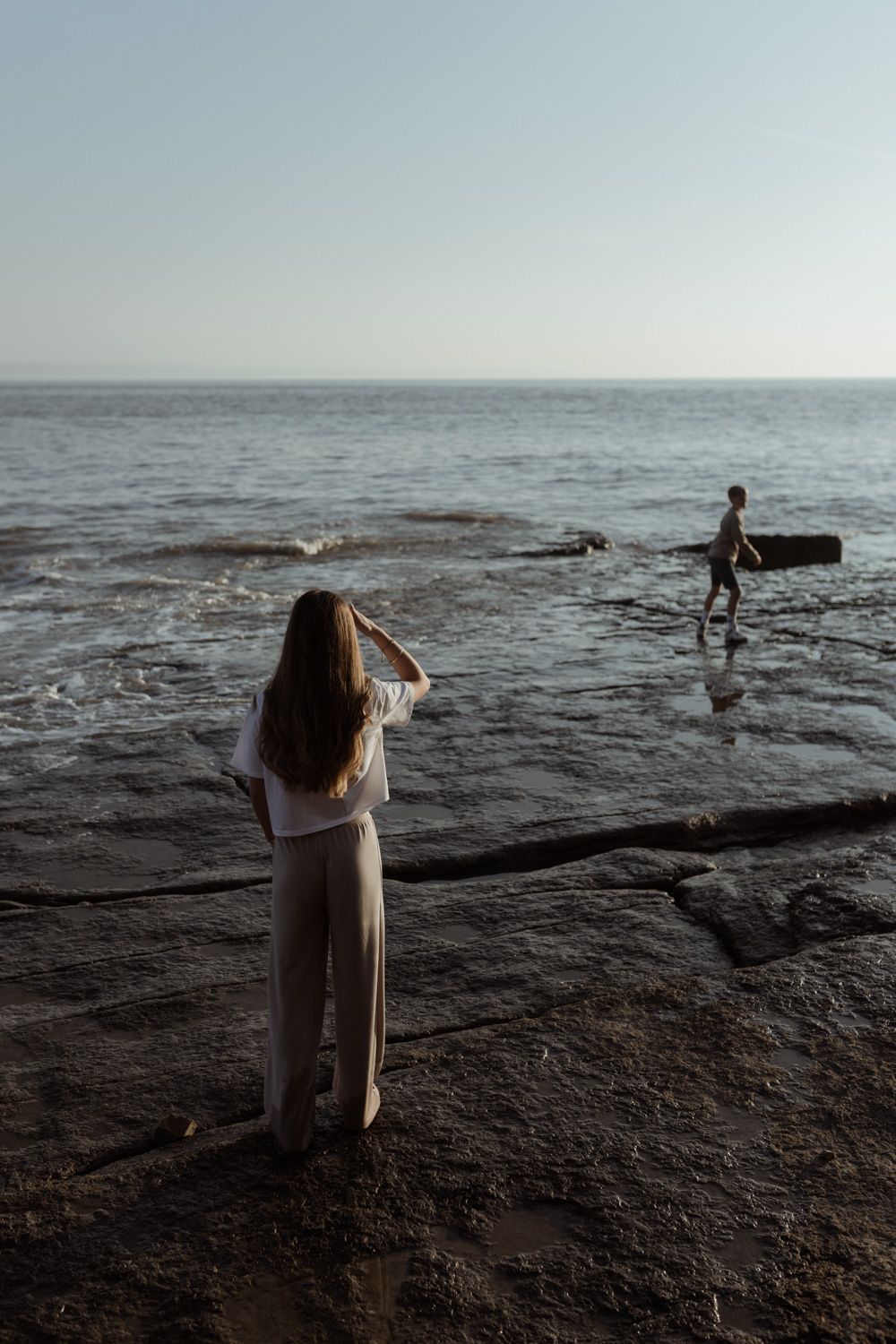 Two people exploring rocky coastline during golden hour.