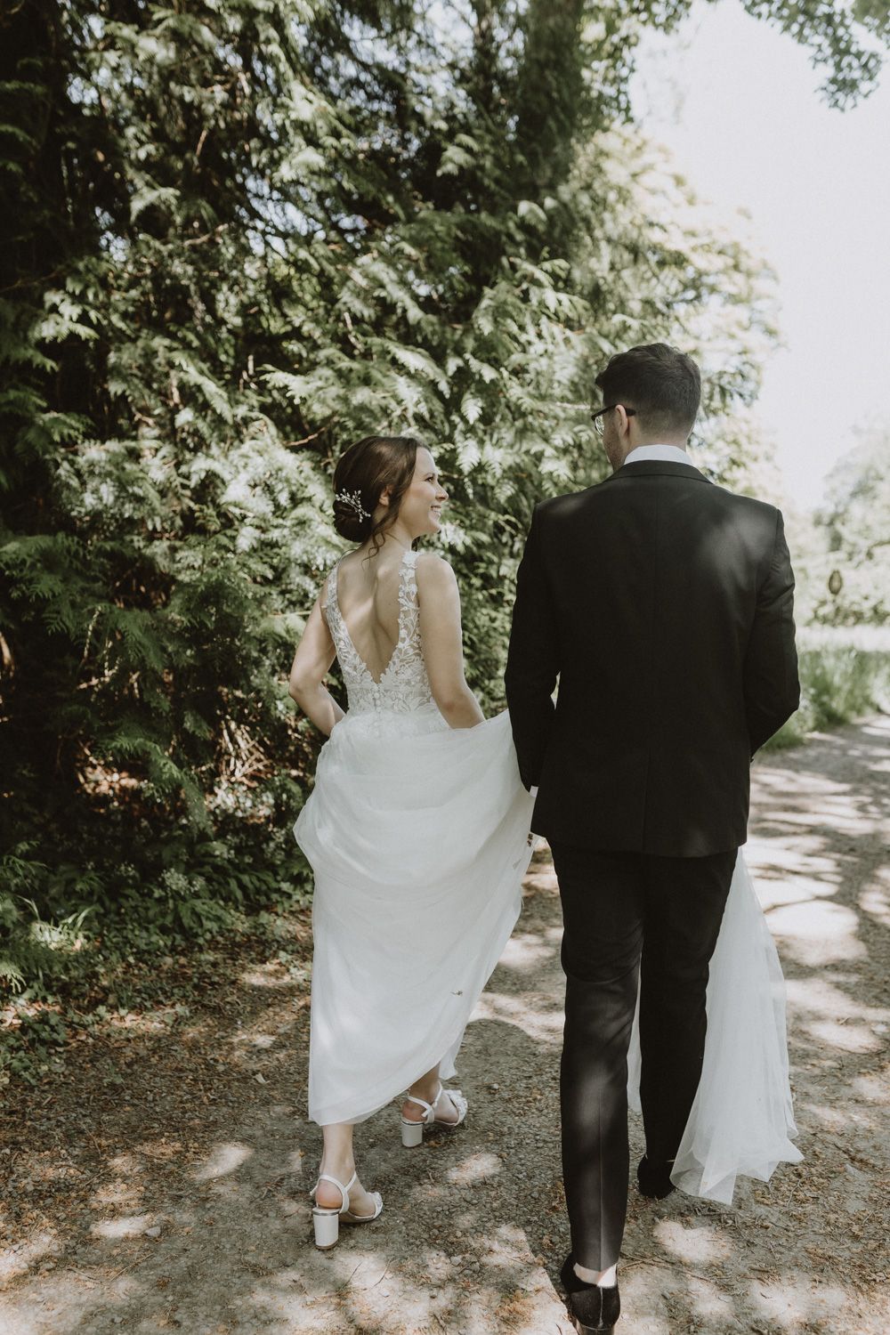 Newlyweds walking hand in hand down a tree-lined path on their wedding day.